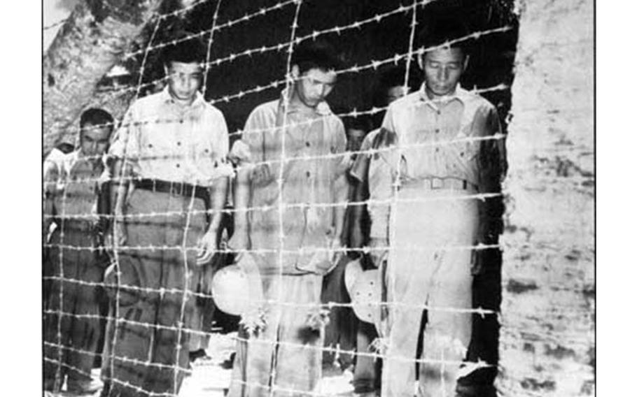 In a camp in Guam, prisoners of war bow their heads as they hear a radio broadcast of Japanese Emperor Hirohito announcing the surrender of Japan in World War II. Photo courtesy of War in the Pacific National Historic Park