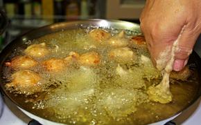 Squeezing the bonelos dough into the oil.