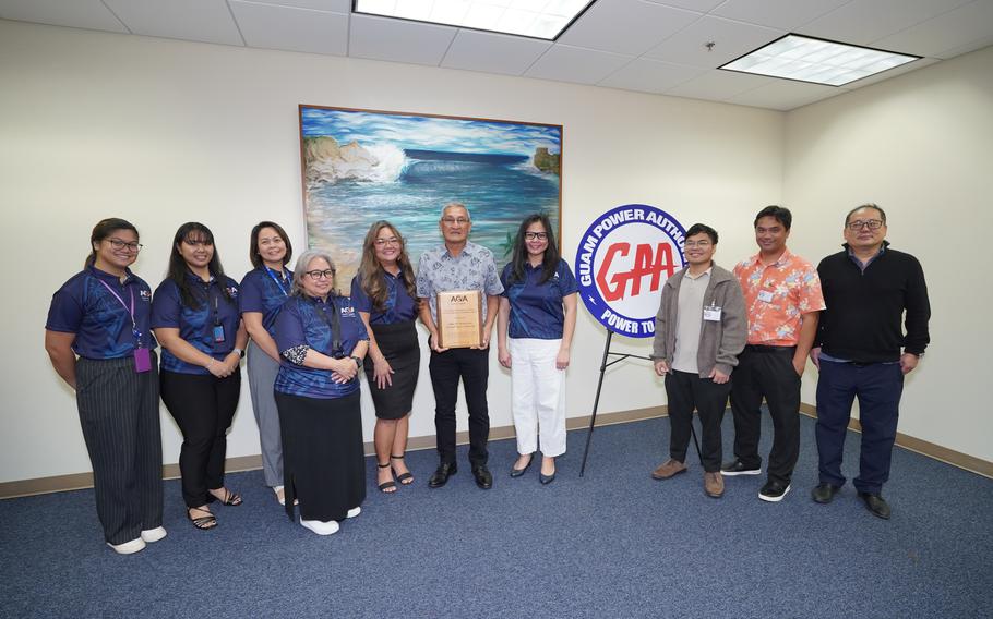 GPA GM John M. Benavente, P.E. holds the award by the wall. some other people are standing beside him.