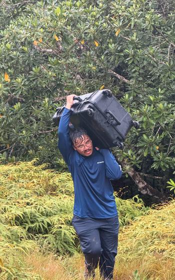 Thomas Torres II hauls a drone case in rainy weather during a mapping mission in Aimeliik, Palau.