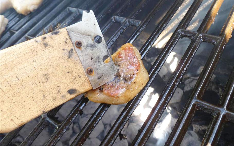 A person is rubbing the fat chunk across the grill grates with a grill brush until they are clean.
