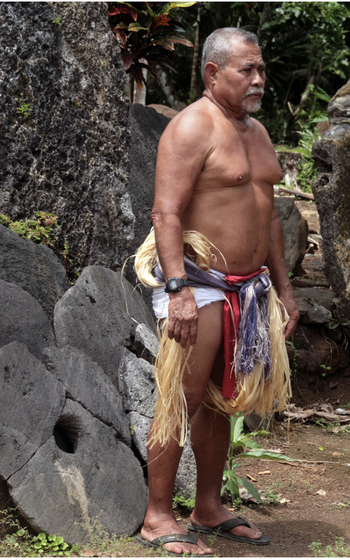 Yapese man wearing traditional thu’u and standing in front of stone money.