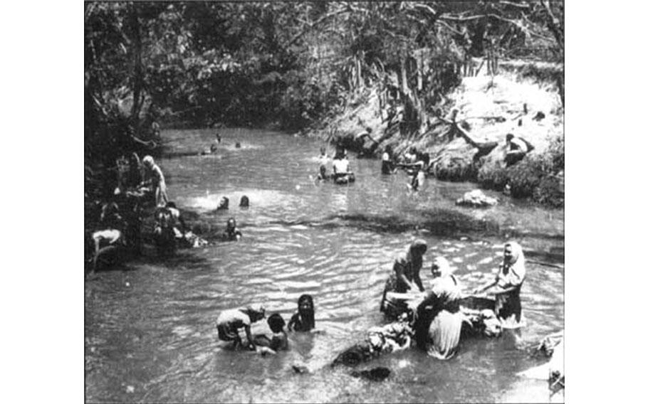 People forced to camp in Manengon used the Ylig River for a water source. In the photo, women are washing clothes as children play in the river’s waters. People from throughout Guam camped at Manengon under Japanese order.