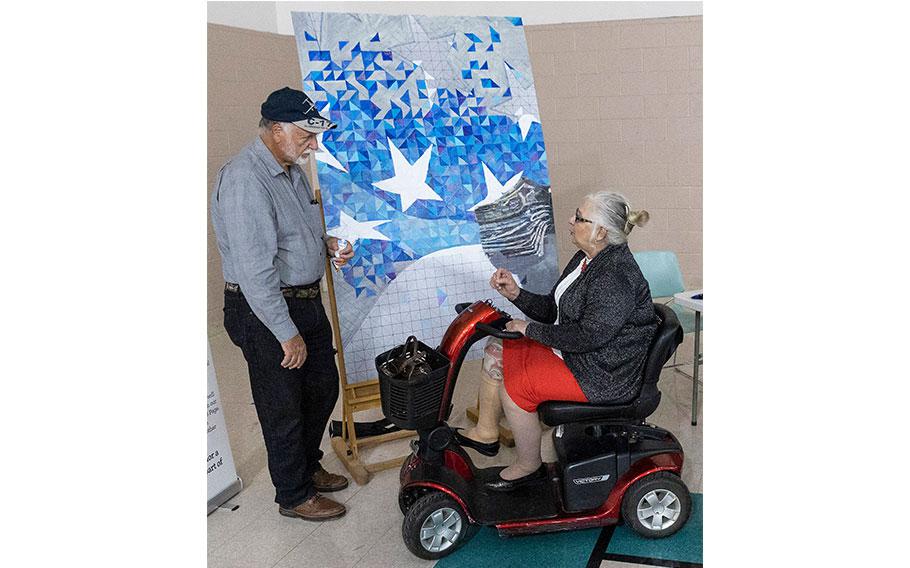 a woman on electric wheelchair is painting and a man is beside her.