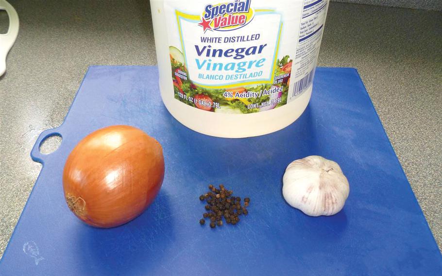 Vinegar, onions, garlic, etc, are on a cutting board.